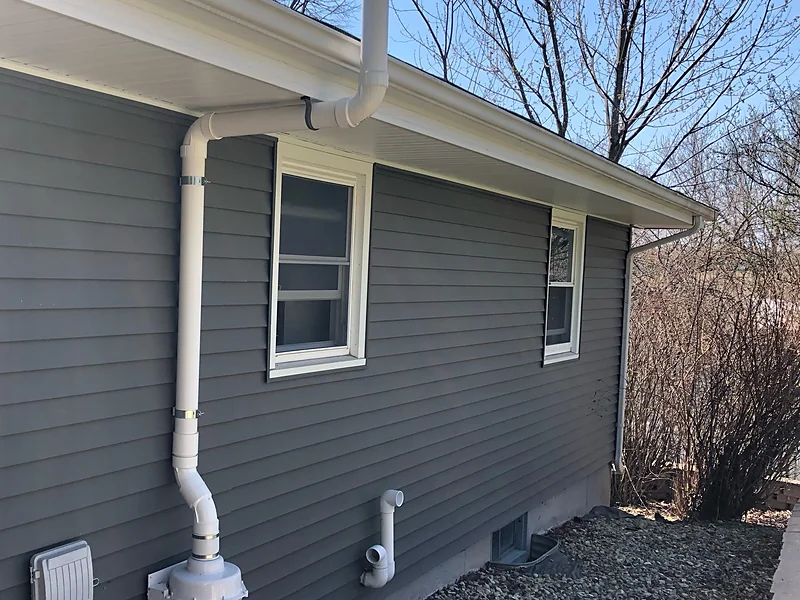 A complete exterior radon system on a home, running from the wall penetration past the fan and up above the roofline